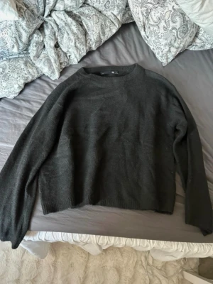 Svart stickad tröja - En enkel och stilren svart stickad tröja med rund hals och långa ärmar. Tröjan har en rak passform och ribbstickade muddar vid ärmslut och nederkant. Perfekt att matcha med jeans eller kjol.