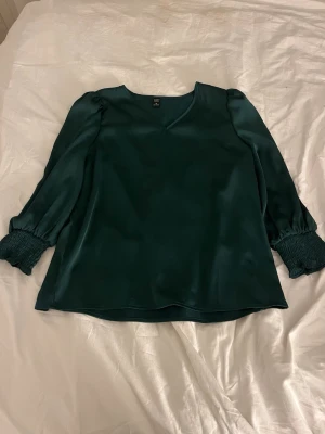 Mörkgrön satinblus med v-ringning  - Stilren mörkgrön blus i glansigt satintyg från emery rosé. Super fin och i väldigt bra skick . 