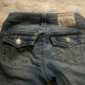 True Religion bootcut jeans blå - Säljer ett par blå bootcut jeans från True Religion med ikoniska kontrastsömmar och stora ficklock bak med silverfärgade knappar. Jeansen har låg midja och klassisk femficksdesign. Materialet är denim i bomull med snygg tvätt.