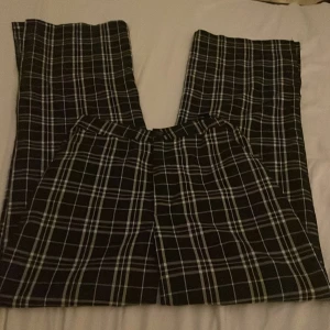 Svarta rutiga byxor  med vida ben(slits) - Snygga svarta rutiga byxor  med vitt rutmönster och vida ben. Byxorna har hög midja. Perfekta för dig som gillar en trendig och avslappnad stil. Materialet är bomull med lite stretch för extra komfort.Fusk fickor bak.