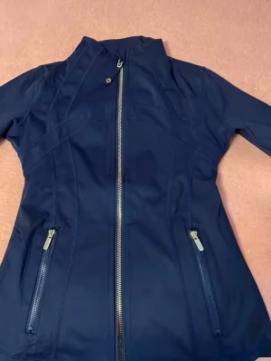 Marinblå define jacket Lululemon - Snygg marinblå vindjacka från Lululemon med figurnära passform och hög krage. Jackan har snedställd dragkedja framtill och två fickor med dragkedja. Tillverkad i ett lätt, vindtätt material som passar perfekt för blåsiga dagar. Size 2