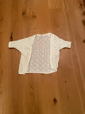 Vit virkad kofta  - Söt vit kofta från UNIQ MINI i virkad stil med  korta ärmar. Perfekt att slänga över en topp för en luftig och trendig look. Koftan har en avslappnad passform och är gjord i ett mjukt material. Skulle säga att den passar de flest, men beror på hur tajt eller pösig man vill ha den🩷