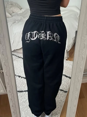 Hidden Cult - Svarta Hidden Cult mjukisbyxor med elastisk midja och snörning framtill. Storlek S i fint skick. På baksidan finns en stor strassdekor med texten 'NASTY' i gotisk stil. Byxorna har en loose passform och är tillverkade i mjukt bomullsmaterial, perfekta för chill dagar. Har även tillhörande hoodie i en annan annons 🖤