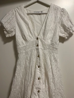 Vit klänning  - Vit broderad klänning med bruna knappar från nakd. Super fin och passa perfekt till sommaren eller studenten. Översta knappen har några trådar som sticker ut men klipper man dem ser den ut som ny. Skicket är annars som nu!