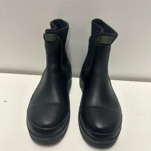 Svarta chunky kängor  från tretorn med resår 40 - Snygga svarta kängor från tretorn med chunky sula och resår vid ankeln. De har en högre skaftmodell och grönt band upptill för enkel påtagning. Tillverkade i ett glansigt syntetmaterial som ger en modern look.