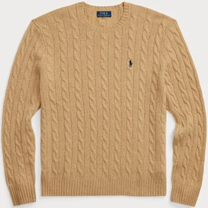 Beige kabelstickad tröja Polo Ralph Lauren - Kabelstickad beige tröja från Polo Ralph Lauren med rund halsringning och broderad marinblå logga på bröstet. Tröjan har ribbade muddar och är tillverkad i mjukt material som ger en klassisk och stilren look.