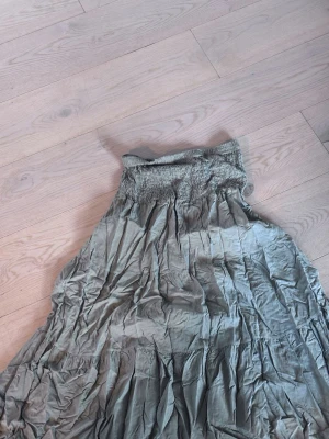 Grå kortklänning från Ezence - Säljer en grå kortklänning från Ezence med smockad midja och lätt rynkad design. Klänningen har en luftig och avslappnad passform, perfekt för varmare dagar. Materialet känns mjukt och bekvämt mot huden.