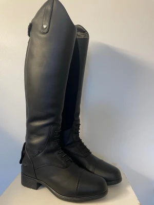 Svarta ridstövlar i läder Ariat - Ariat varma vinterridstövlar stl 37  Varma, fodrade med Primaloft (Thinsulate) 200 g- foder och vattentäta.  Storlek 37M, se bild för exakta mått. Står short men upplevs normala för 165-cm-människa.   Är både varma och sköna att rida i och står emot iskylan både i tån, runt foten och runt benet.  Bra stöd i stigbygeln.   Bara använda för ridning (inget stallarbete) ett fåtal gånger när det varit riktigt kallt. Har stått varmt året om. Perfekt skick, dragkedjor och knappar fungerar som nya. Enda 