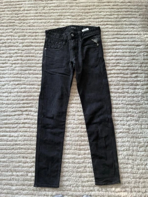 Svarta skinny jeans från Replay - Säljer ett par svarta skinny jeans från Replay med klassisk femficksdesign och silverfärgade detaljer. Jeansen har en smal passform och är tillverkade i stretchigt denimtyg för extra komfort. Perfekta för en trendig och avslappnad look.