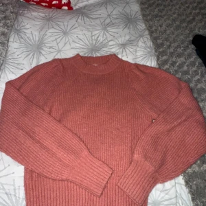 Rosa stickad tröja från Monki XS - Mysig stickad tröja från Monki i en snygg rosa färg. Modellen har rund hals, ribbade muddar och långärmade puffärmar som ger en cool siluett. Perfekt för att hålla sig varm och ändå se trendig ut. Storlek XS.