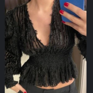 Svart blus med v-ringning från NA-KD - Säljer en svart blus från NA-KD med transparent tyg och fluffiga ränder. Blusen har djup v-ringning, långärmade puffärmar och smockad midja som ger en snygg siluett super snygg för fest❤️