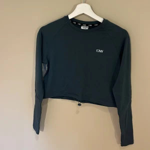 Mörkgrön croppad tröja från ICANIWILL - Snygg mörkgrön croppad tröja från ICANIWILL med lång ärm och diskret logga på bröstet. Tröjan har dragsko nertill för justerbar passform och är tillverkad i mjuk bomullsblandning med polyester och lite stretch. Väldigt skön och perfekt för en snygg träningslook. Knappt använd (1 gång) och inga defekter💪🏼💪🏼