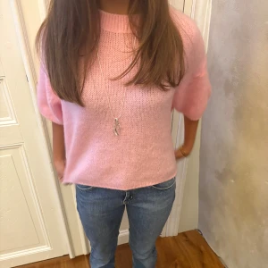 Ljusrosa stickad tröja med puffärm - Superfin ljusrosa stickad tröja med korta puffärmar och rund hals. Tröjan har en loose passform och är perfekt för dig som gillar en söt och avslappnad stil. Mjuk och skön, passar perfekt till jeans eller kjol.