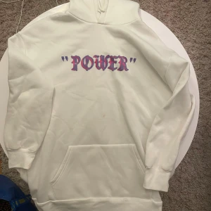Vit hoodie med POWER-tryck och vingar - Säljer en vit hoodie med lila och rosa POWER-tryck på bröstet och stora färgglada vingar på ryggen. Hoodien har huva, magficka och långa ärmar. Perfekt statement-plagg för dig som vill sticka ut. Finns ingen lapp så osäker på storlek men skulle säga M-L❤️