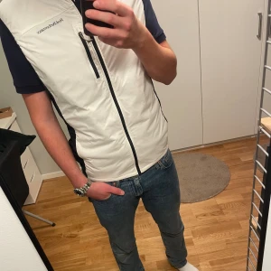 (HELT NY) Peak Performance dunväst  - HELT NY dunväst från Peak Performance med svarta detaljer och dragkedja framtill. Västen har en hög krage, bröstficka med dragkedja. Sportig look och stilren design som funkar året runt.