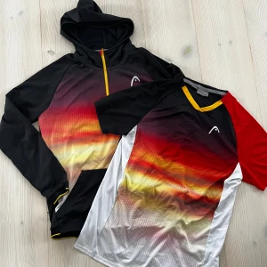 Head tränings  hoodie och t-shirt  - Säljer en sportig hoodie med huva och half zip samt en matchande t-shirt från Head. Båda har ett coolt färgskiftande mönster i svart, rött, gult och vitt. Hoodien har långa ärmar och dragkedja, t-shirten har kort ärm och gul kant vid halsen. Hoodie stl 164 och T-shirt stl 176 men upplevs lika i storleken. Mycket fint skick. Djur- och rökfritt hem. hoodie 175:- T-shirt 125:-, båda för 250:-