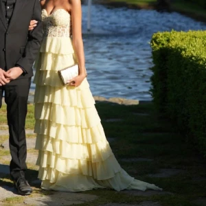 Balklänning  - Superfin ljusgul långklänning med axelbandslös, hjärtformad överdel i spets och flera lager volanger i kjolen. Jag är 170, och bär vanligtvis xs/s. I ryggen är det som en korsett som man kan spänna hur mycket man vill.