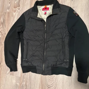 Parajumper cardigan - Säljer en svart fleecejacka från Parajumpers med dragkedja och ribbade muddar. Jackan har en quiltad design och är perfekt för kyligare dagar. Den har en snygg broderad detalj på ärmen.