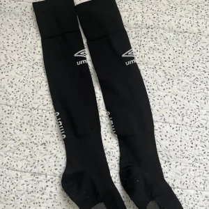 Svarta Umbro fotbollsstrumpor  - Svarta fotbollstrumpor från Umbro med vit logga på sidan. Materialet är mjukt och stretchigt