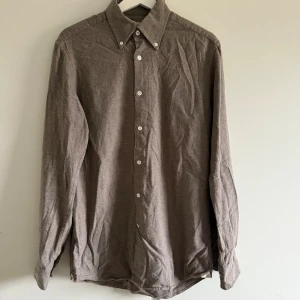 Brun skjorta från Morris i bomull - Snygg brun skjorta från Morris med klassisk krage och vita knappar. Skjortan är tillverkad i mjuk bomull och har lång ärm. Perfekt för dig som gillar stilrena och tidlösa plagg.