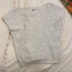 Beige stickad ärmlös/off shouldee tröja från Nelly - Supermjuk och stickad ärmlös tröja från Nelly i en ljusbeige ton. Tröjan har en avslappnad passform med ribbad kant nertill