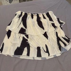 Plisserad kortkjol med zebramönster - Superfin plisserad topp med svartvitt zebramönster och volangkant. Toppen har resår i och är gjord i ett lätt, glansigt material som ger en snygg och flowy look.