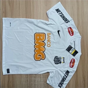 Santos Neymar Jr 11 vit matchtröja Nike - Säljer en officiell Santos FC fotbollströja med Neymar Jr och nummer 11 på ryggen. Tröjan är vit med svarta och orange tryck, korta ärmar och rund hals. Märkt med Nike-logga och flera sponsorer. Tillverkad i lätt, ventilerande polyester.
