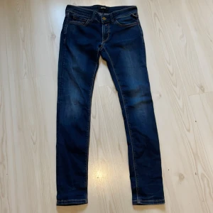 Replay blå skinny jeans, W28 L30 - Snygga mörkblå jeans från Replay med skinny passform och klassisk femficksdesign. Jeansen har kontrastsömmar, guldfärgad knapp och är tillverkade i stretchigt denim för skön komfort. Perfekt för dig som gillar en smal siluett och stilren look.