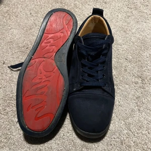 Mörkblå sneakers från Christian Louboutin - Snygga mörkblå sneakers från Christian Louboutin med klassisk röd sula och diskret broderad logga på hälen. Skorna har rund tå, platt sula och snörning. Utsidan är i mocka och insidan i skinn, vilket ger en lyxig känsla. Perfekt för dig som gillar exklusiva detaljer. Tveka inte på att höra av dig vid frågor, priset är ej hugget i sten😊