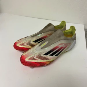 Adidas F50 fotbollsskor i rött och gult - Säljer ett par Adidas F50 fotbollsskor med en futuristisk design i vitt, rött, gult och svarta detaljer. Skorna har metall- och plastdobbar, låg profil och är tillverkade i lätt syntetmaterial. Perfekta för dig som vill sticka ut på planen.väldigt bra skick har inte andvänt mycket .