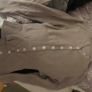 Beige kofta med knappar  - Säljer en beige kofta  med långa ärmar och snygga vita knappar framtill. Koftan har ribbade partier nedtill och vid ärmsluten, vilket ger en schysst kontrast. Perfekt för lager-på-lager och enkel att matcha med det mesta.