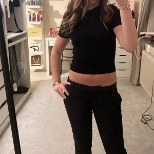 Svart stickad topp från Gina Tricot - En svart, croppad stickad topp från Gina Tricot med rund hals och korta ärmar. Enkel och stilren modell som är lätt att matcha till olika outfits. Perfekt för dig som gillar en clean och klassisk look. Den är ribbad i materialet. 