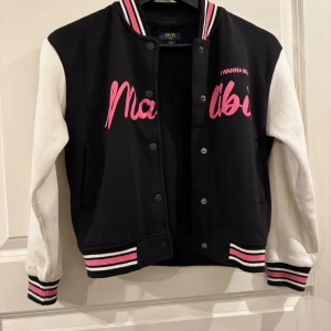 Svart och vit bomberjacka OVS Kids - Snygg svart och vit bomberjacka från OVS Kids med långa vita ärmar, svart kropp och coola rosa detaljer. Jackan har tryckknappar, randiga muddar i svart, vitt och rosa samt tryckt text framtill. Perfekt för dig som vill sticka ut med en sportig look. Pris kan diskuteras!