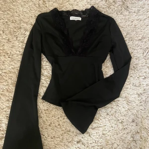 Svart långärmad topp med spets - Snygg svart långärmad topp från Venderby’s Figurnära topp med markerad midja och utsvängda ärmar. Storlek Xs/S
