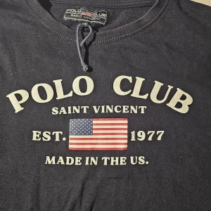 Svart långärmad tröja Polo Club - Svart långärmad tröja från Polo Club Saint Vincent med tryck framtill i vitt och amerikansk flagga. Rund halsringning med snörning och ribbade muddar. Perfekt för dig som gillar klassisk och sportig stil.