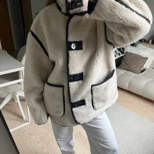Beige teddyjacka med svarta detaljer - Säljer en beige teddyjacka med svarta kantband och stora knappar framtill. Jackan har två fickor, hög krage och är fodrad med svart tyg på insidan. Aldrig använd! 😊