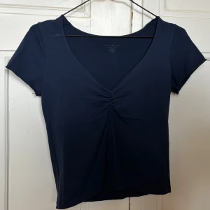 Mörkblå topp med v-ringning Brandy Melville - Snygg mörkblå topp från Brandy Melville med v-ringad hals och rynkad detalj framtill. Kortärmad och figurnära passform, tillverkad i mjuk bomull. Perfekt för dig som gillar enkel men stilren look. 💞onesize men passar som en S