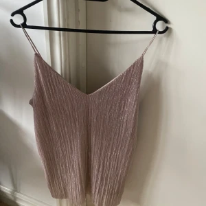 Glittrig ljusrosa linnetopp från Gina Tricot - Säljer en glittrig ljusrosa linnetopp från Gina Tricot i storlek XS. Toppen har smala axelband, v-ringad hals och ett snyggt plisserat tyg som ger extra shimmer. Perfekt för att lyfta din look med lite extra glam.