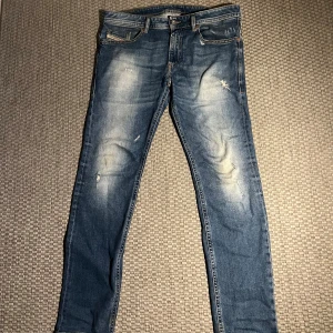 Blåa diesel jeans me snygg tvätt  - Säljer ett par snygga blå jeans från Diesel med klassisk tvättad finish och slitningar. Jeansen har raka ben, normal passform och klassiska fem fickor. Materialet är robust denim i bomull och de har snygga kontrastsömmar. Perfekta för en avslappnad stil. På 3edje bilden ser man slitage vid skrevet men är inget farligt. Pris kan diskuteras. Storlek. W33 L 32✅