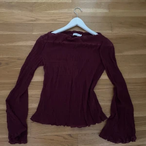 Vinröd långärmad blus med volangärm - Säljer en vinröd långärmad blus med lätt rynkat tyg och utsvängda volangärmar. Toppen har en figurnära passform och vågig kant nertill och vid ärmslut. 