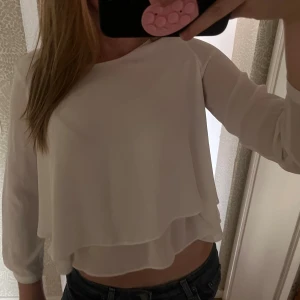 Vit blus med lager på lager - Säljer en vit blus med lager på lager-effekt och trekvartsärmar. Blusen har en luftig och flowy passform med rund halsringning och är tillverkad i ett tunt, lätt material som ger en snygg och stilren look.