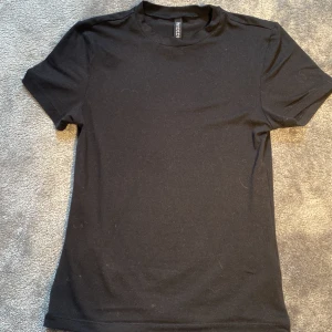 Svart basic t-shirt från H&M Divided - En svart, enkel t-shirt från H&M Divided med rund halsringning och korta ärmar. Modellen är klassisk och passar perfekt till jeans eller kjol. Tillverkad i mjuk bomull för en skön känsla hela dagen.