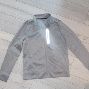 Grå sportig jacka från Pier One - Grå sportjacka från Pier One med hel dragkedja och ståkrage. Jackan har en reflekterande bröstficka med dragkedja och två sidofickor. Tillverkad i mjuk polyester, perfekt för aktiva dagar. Enkel och stilren design som funkar till det mesta. HELT NY! 