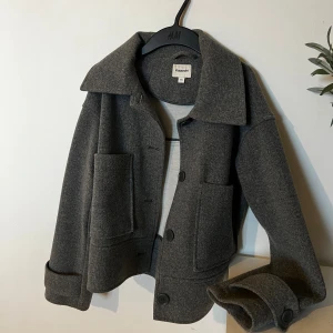 Grå ulljacka från Kappahl - Grå jacka från Kappahl i ullblandning med stora fickor framtill, bred krage och knäppning med knappar. Jackan har en lite croppad passform och långa ärmar med snygga manschetter. Sällan använd.