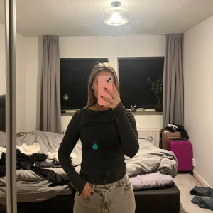 Mörkgrå långärmad topp - Säljer en mörkgrå långärmad topp med tight passform, rund hals och en liten slits längst ner på ärmen. Materialet känns mjukt och stretchigt, perfekt för dig som gillar en enkel men stilren look. Passar till jeans eller kjol och är lätt att matcha med andra plagg.