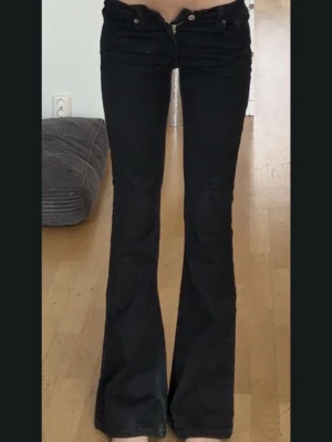 Svarta bootcut jeans från Zara - Säljer ett par svarta bootcut jeans från Zara i storlek 34. Jeansen har låg midja, klassisk dragkedja och knapp framtill samt utsvängda ben. Materialet är mjukt och stretchigt för en bekväm passform.