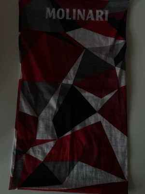 Geometrisk halsduk från Molinari - Snygg halsduk med geometriskt mönster i rött, svart, grått och vitt från Molinari. Perfekt accessoar för att lyfta din outfit med en modern touch. Halsduken har tryckt logga upptill och är tillverkad i ett mjukt tyg.