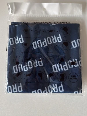 Mörkblå multifunktionell halsvärmare PROPUD - Säljer en mörkblå multifunktionell halsvärmare från PROPUD. Den kan användas på flera olika sätt, till exempel som halsduk, pannband eller mössa. Materialet är mjukt och stretchigt, perfekt för att anpassa efter din stil. Tryckt med vit PROPUD-logga över hela tyget.