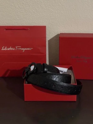 Svart läderbälte Salvatore Ferragamo - Snyggt svart bälte från Salvatore Ferragamo i präglat läder med klassiskt mönster och rundad metallspänne. Kommer i originalförpackning med dustbag och ask. Perfekt accessoar för att lyfta din outfit.
