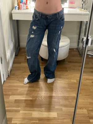 Blå baggy jeans med slitningar - Säljer ett par blå baggy jeans med slitna detaljer. Jeansen har låg midja. 47 cm i midjan tvärs över och 80 cm i innerbenslängd, har sytt in tyg vid smalbenet för att få dom mera flare, säljer då dom är för stora på mig💕💕